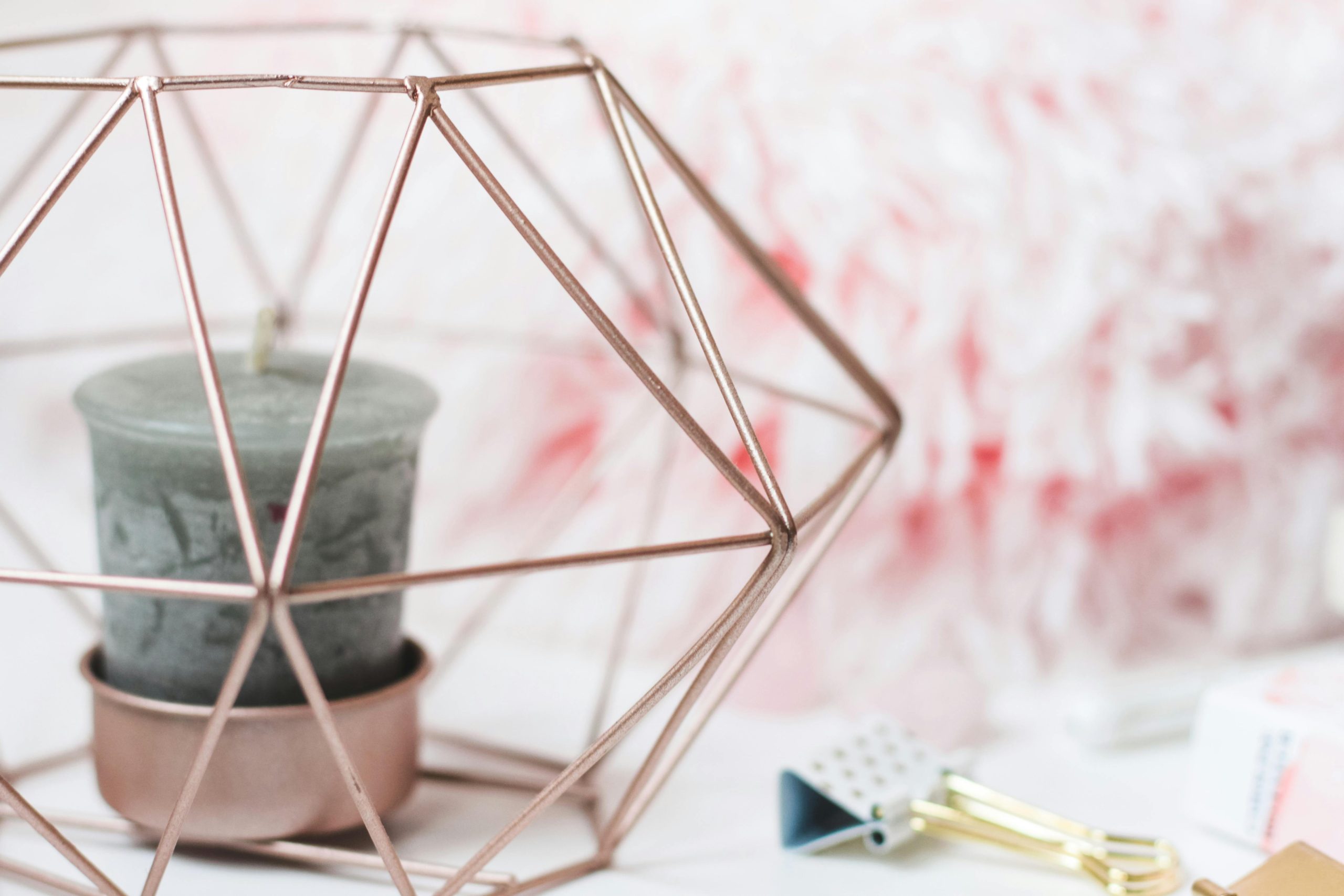 Rose gold geometric metal candle holder with a decorative candle inside, on a light background.