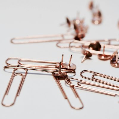 Aesthetic rose gold paperclips and thumb tacks on a white background, ideal for office decor or supplies imagery.